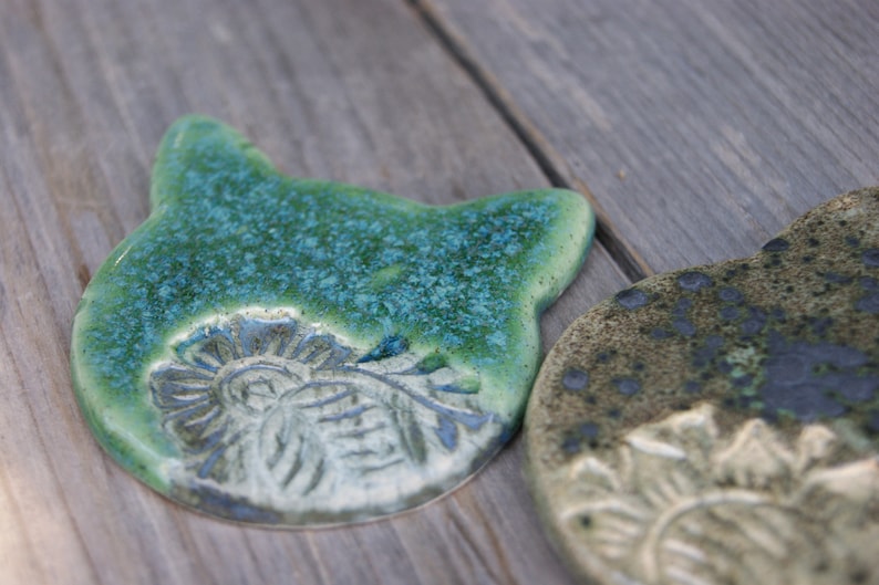 Puede incluir: Dos posavasos de cer&aacute;mica con un esmalte verde y azul. Los posavasos presentan un dise&ntilde;o en relieve de una flor.