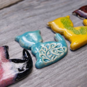 May include: Five ceramic cat figurines in various colors, including pink, black, blue, yellow, and brown. Each figurine has a unique design and glaze.