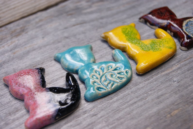 May include: Five ceramic cat figurines in various colors, including pink, black, blue, yellow, and brown. Each figurine has a unique design and glaze.
