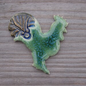 May include: A ceramic rooster figurine with a green and blue glaze. The rooster has a detailed crest and a textured body.
