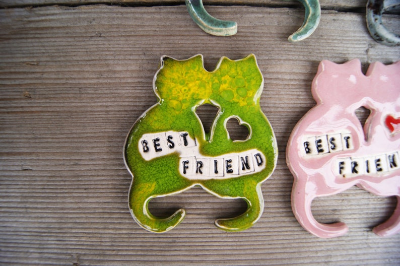 Puede incluir: Dos figuritas de cer&aacute;mica de gatos, una verde y otra rosa, est&aacute;n unidas. Est&aacute;n decoradas con azulejos blancos que deletrean "Best Friend".