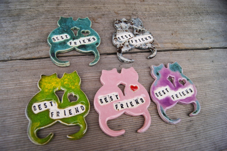Puede incluir: Cinco figuritas de cer&aacute;mica de gatos, cada una con un esmalte de color diferente. Los gatos est&aacute;n en parejas, con sus colas entrelazadas. Cada pareja tiene las palabras "Mejor amigo" escritas en letras negras.