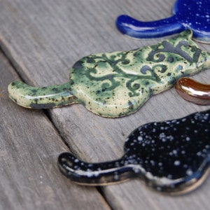 May include: Five ceramic cat figurines in different colors and patterns. The cats are all in a similar pose, with their tails curled around their bodies. The cats are made of a smooth, glazed ceramic and have a variety of colors and patterns.