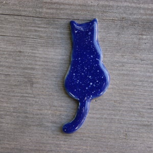 May include: A blue ceramic cat figurine with a speckled finish. The cat is facing away from the viewer with its tail curled around its body.