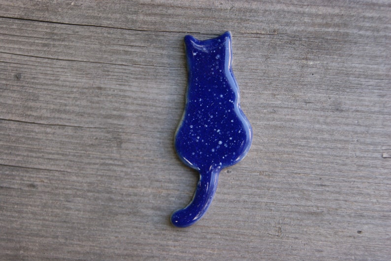 May include: A blue ceramic cat figurine with a speckled finish. The cat is facing away from the viewer with its tail curled around its body.