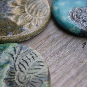 Puede incluir: Tres posavasos de cer&aacute;mica con un esmalte verde y azul. Cada posavasos presenta un dise&ntilde;o diferente con un patr&oacute;n en relieve.