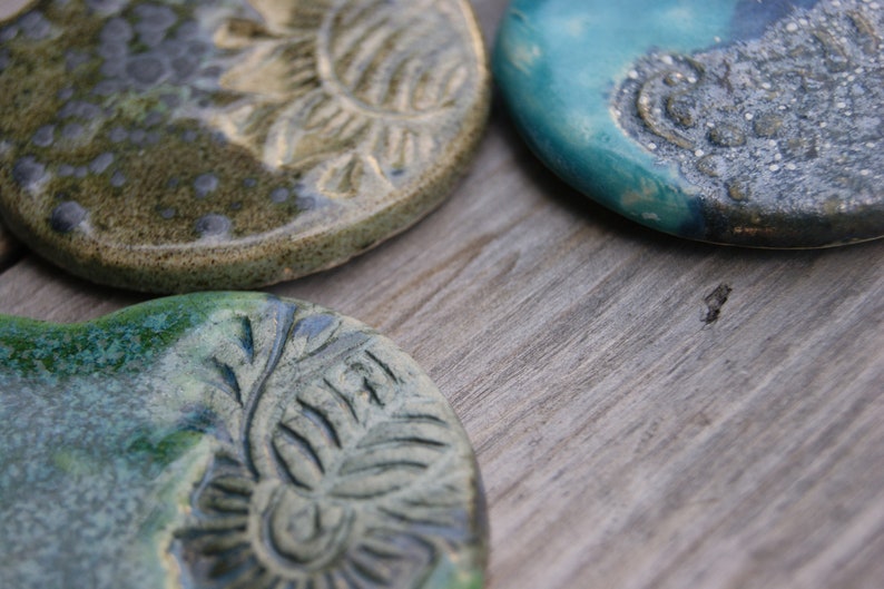 Puede incluir: Tres posavasos de cer&aacute;mica con un esmalte verde y azul. Cada posavasos presenta un dise&ntilde;o diferente con un patr&oacute;n en relieve.