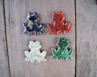 May include: Four ceramic frog figurines in different colors: blue, red, green, and white. Each frog is sitting with its legs outstretched.