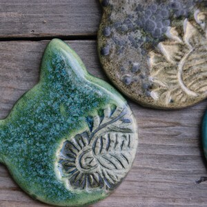 Puede incluir: Tres adornos de cer&aacute;mica con diferentes dise&ntilde;os. Uno es verde con un patr&oacute;n floral, otro es gris con un dise&ntilde;o de girasol y el &uacute;ltimo es azul con un patr&oacute;n de remolino.