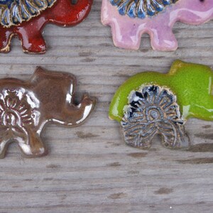 May include: Five ceramic elephant figurines with intricate floral designs. The elephants are in various colors, including brown, red, pink, and green.