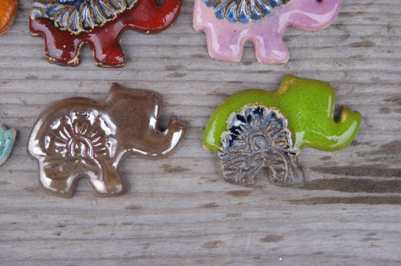 May include: Five ceramic elephant figurines with intricate floral designs. The elephants are in various colors, including brown, red, pink, and green.