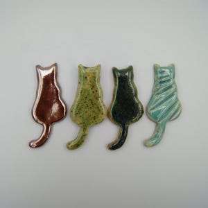 May include: Four ceramic cat figurines in different colors and patterns. The cats are facing away from the viewer and have a glazed finish.