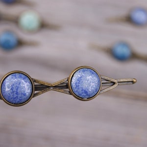 Puede incluir: Un par de pinzas para el pelo de cer&aacute;mica marmoleada azul y blanca con un marco de metal bronce. Las pinzas tienen forma de diamante con una sola pinza en cada extremo.
