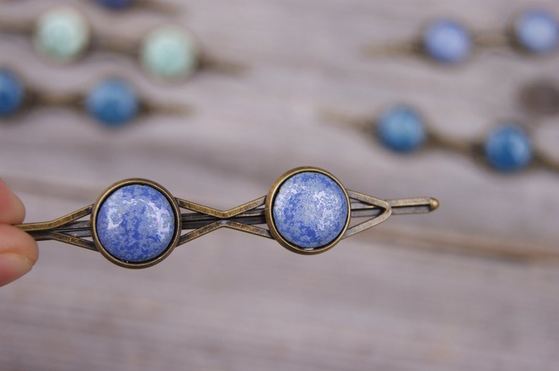 Puede incluir: Un par de pinzas para el pelo de cer&aacute;mica marmoleada azul y blanca con un marco de metal bronce. Las pinzas tienen forma de diamante con una sola pinza en cada extremo.