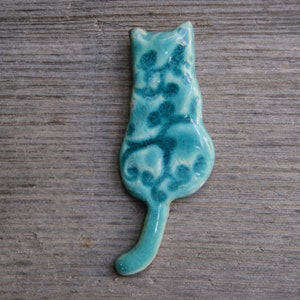 May include: A teal blue ceramic cat figurine with a white floral design. The cat is sitting with its tail curled around its body.