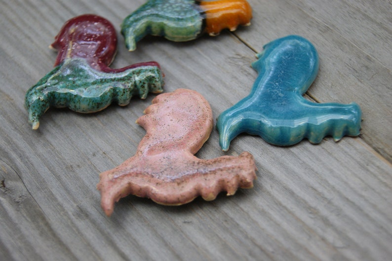 May include: Four ceramic figurines in the shape of a bird, each painted in a different color: green, blue, pink, and orange. The figurines are arranged on a wooden surface.