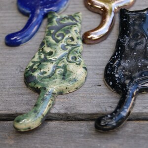 May include: Four ceramic cat figurines in different colors and patterns. One is blue, one is gold, one is green with a floral pattern, and one is black with white speckles.
