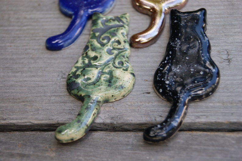 May include: Four ceramic cat figurines in different colors and patterns. One is blue, one is gold, one is green with a floral pattern, and one is black with white speckles.
