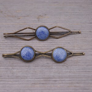 Puede incluir: Dos pinzas para el pelo de bronce con piedras redondas azules marmoleadas. Las pinzas tienen un dise&ntilde;o geom&eacute;trico.