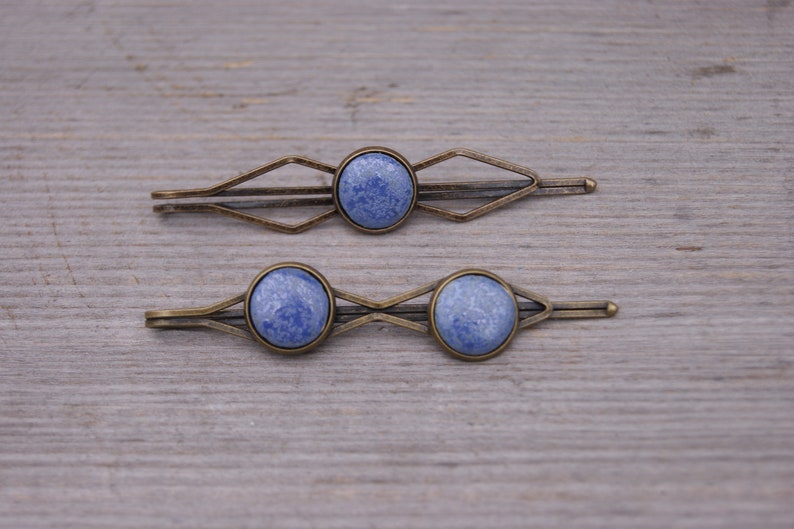 Puede incluir: Dos pinzas para el pelo de bronce con piedras redondas azules marmoleadas. Las pinzas tienen un dise&ntilde;o geom&eacute;trico.