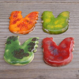 Op de afbeelding: Vier keramische kippenfiguren in verschillende kleuren. De kippen zijn oranje, groen, geel en rood.