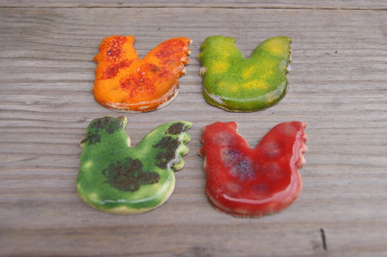 Op de afbeelding: Vier keramische kippenfiguren in verschillende kleuren. De kippen zijn oranje, groen, geel en rood.