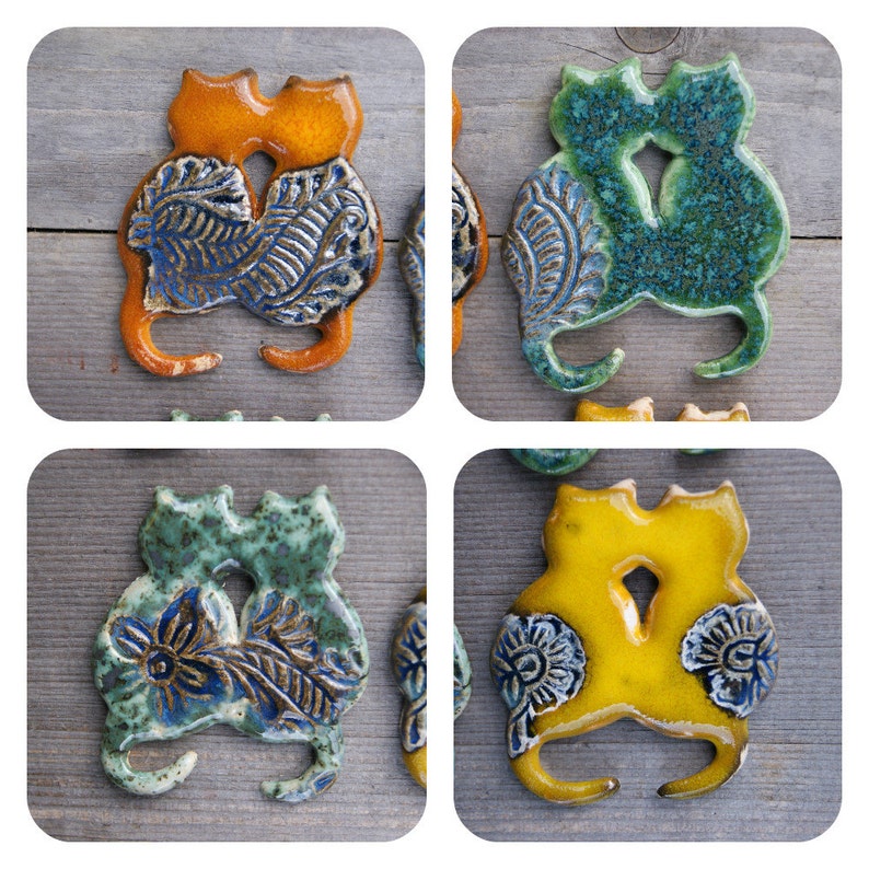 May include: Four ceramic cat figurines, each depicting two cats cuddling. The cats are in different colors: orange, green, blue, and yellow. Each figurine has a detailed floral design.