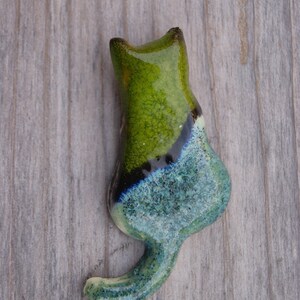 May include: A ceramic cat figurine with a green, blue, and black glaze. The cat is sitting with its tail curled around its body.