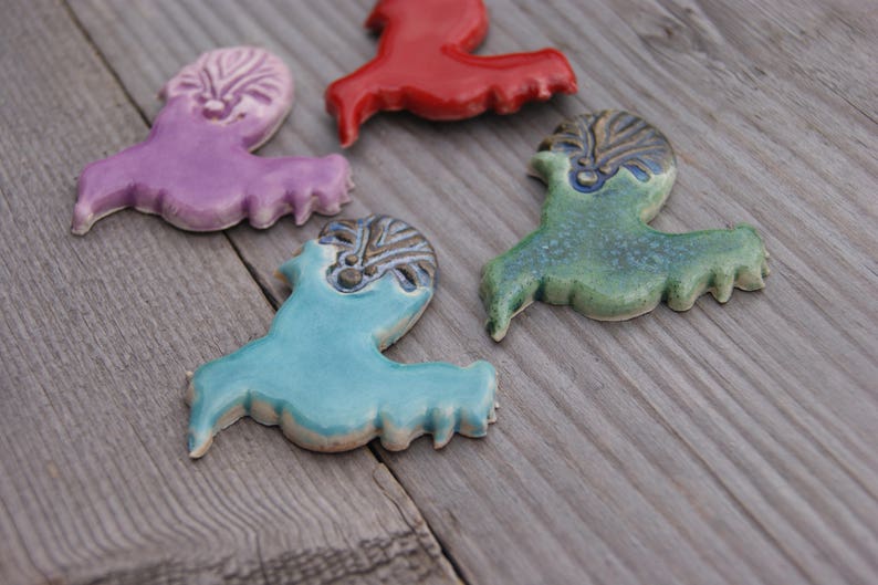 May include: Four ceramic figurines in the shape of birds. The birds are painted in different colors, including purple, red, green, and blue. The birds have detailed designs on their bodies.