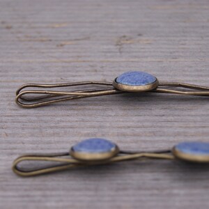 Puede incluir: Dos pinzas para el pelo doradas con detalles de piedras preciosas azules. Las pinzas son sencillas y elegantes, perfectas para a&ntilde;adir un toque de brillo a cualquier peinado.