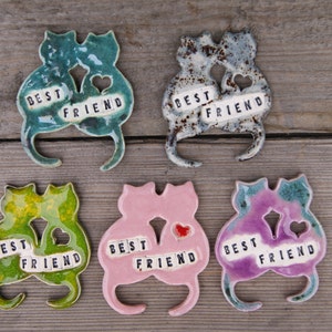 Puede incluir: Cinco figuritas de cer&aacute;mica de gatos, cada una con dos gatos que se miran, con las palabras "Best Friend" escritas en ellas. Los gatos son de diferentes colores: verde, gris, rosa, amarillo y morado.