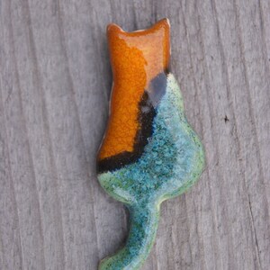 May include: A ceramic cat figurine with a blue, green, and orange glaze. The cat is in a sitting position with its tail curled around its body.