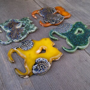 May include: Four ceramic wall hooks in the shape of stylized birds. The hooks are painted in shades of green, yellow, and orange with blue floral designs.