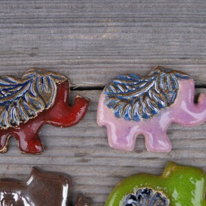 May include: Four ceramic elephant figurines with blue and brown leaf designs. The elephants are in shades of red, pink, brown, and green.