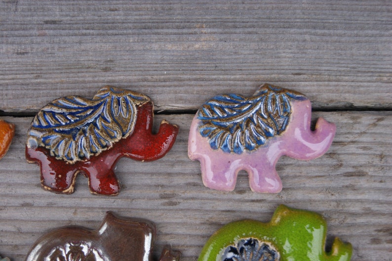 May include: Four ceramic elephant figurines with blue and brown leaf designs. The elephants are in shades of red, pink, brown, and green.