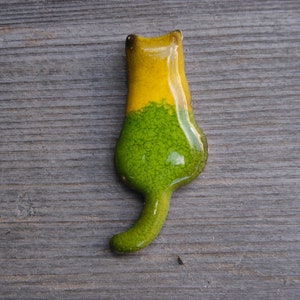 May include: A ceramic cat figurine with a green and yellow glaze. The cat is standing on its hind legs with its tail curled behind it.