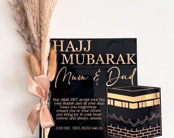 Peut inclure: Plaque noire en acrylique « Hajj Mubarak » avec lettrage doré, avec les mots « Mum & Dad ». La plaque comprend un motif décoratif de la Kaaba et un bouquet de fleurs séchées noué avec un ruban rose. Le texte comprend une prière et la date de juin 2025.