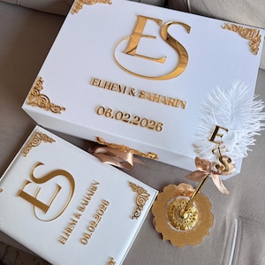 Puede incluir: Caja de regalo de boda blanca con detalles dorados, con las iniciales "ES", los nombres "ELHEM & SAHARIN" y la fecha "06.02.2026". Incluye un libro de visitas a juego y un bolígrafo decorativo.