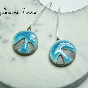 Può includere: Un paio di orecchini pendenti in argento con ciondoli rotondi in ceramica blu e grigia. I ciondoli hanno un design unico con una smaltatura blu chiaro e un centro grigio.