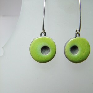 May include: A pair of green ceramic earrings with a silver hook. The earrings are shaped like a donut with a hole in the centre.