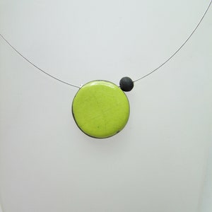 May include: A lime green circle pendant necklace with a black bead accent. The necklace is made of a thin silver chain.