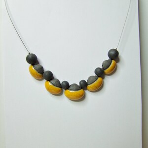 May include: A necklace with a silver chain and yellow and grey ceramic beads. The beads are shaped like half-circles.