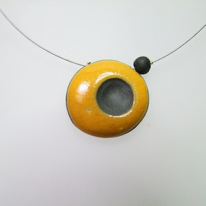May include: A yellow ceramic pendant with a black circle in the centre, hanging from a silver chain.