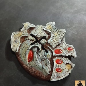 May include: A detailed, fantasy-themed pendant with a brown base and intricate silver-colored detailing. The pendant features red gemstone accents and a stylized design, possibly for cosplay or fantasy enthusiasts.
