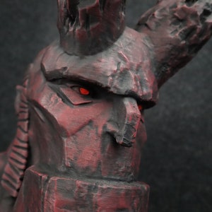 Puede incluir: Primer plano de una escultura de piedra gris oscuro y roja de una criatura con una gran corona dentada y ojos rojos brillantes.