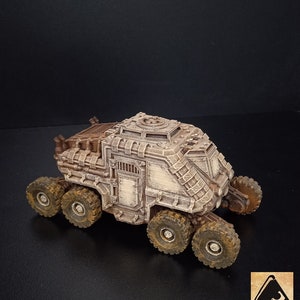May include: A detailed, beige, 3D printed model of a futuristic, armored vehicle with six wheels and a large, rectangular door on the side.