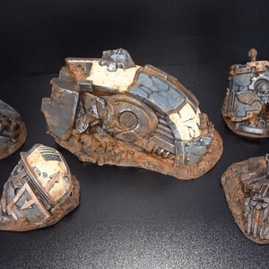 May include: Five pieces of a destroyed, gray and white, metal spaceship model. The pieces are on a brown, dirt-like base.