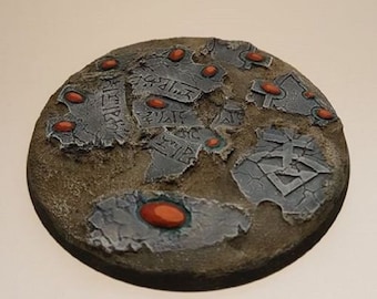 May include: A round, gray and brown base with a cracked, textured surface. The base is decorated with red gems and etched with an inscription.