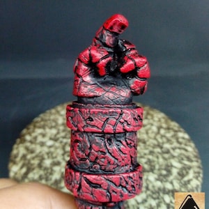 May include: A red and black hand sculpture with a textured surface. The hand is raised with the index finger pointing up.