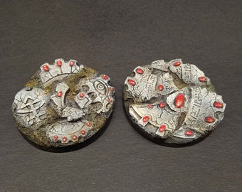 May include: Two round, gray and silver, miniature bases with red gems. The bases are textured and have a worn, aged look.